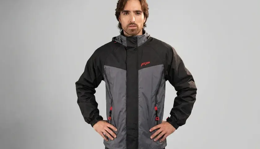 Hombre posando con una prenda impermeable que protege de la lluvia, chaqueta de dos tonos gris y negro con detalles rojos.
