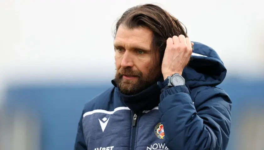 Peter Hyballa, trener Wisły Kraków, poprawia włosy, ubrany w kurtkę z logo klubu.