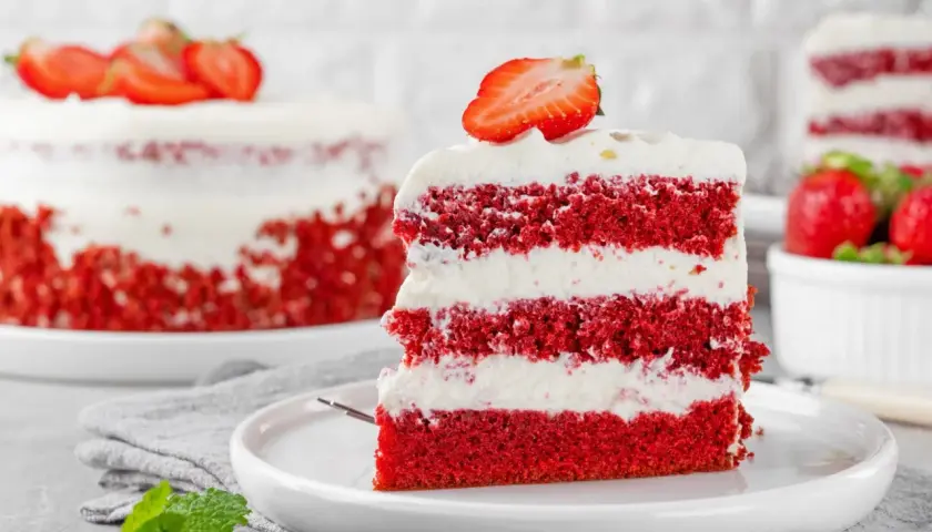 Kawałek tortu red velvet z kremem i truskawkami na talerzu.