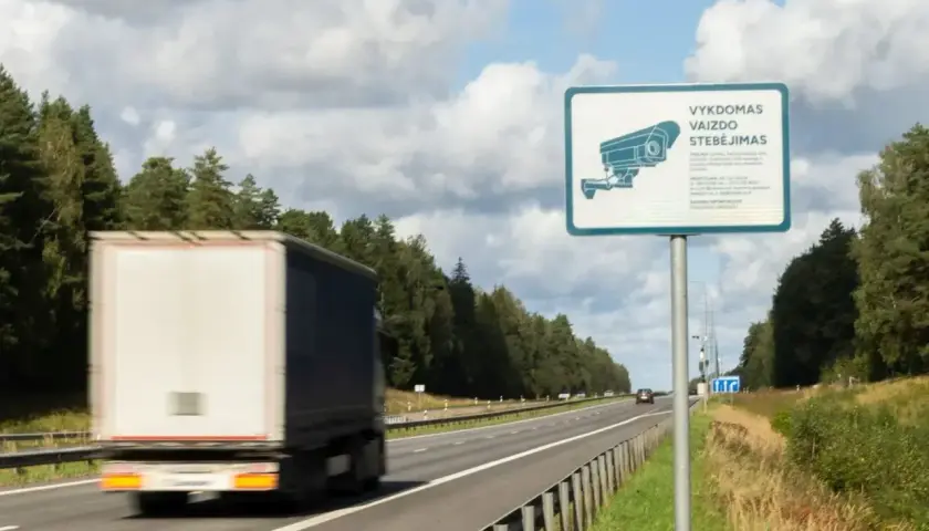 Znak informuje o monitoringu na Litwie. Ciężarówka mija znak z kamerą na autostradzie.