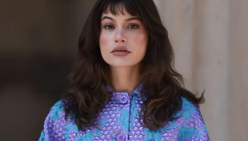 Mujer con melenas cortas con volumen, flequillo y un llamativo abrigo morado y turquesa.