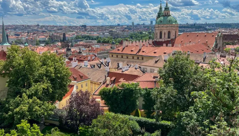 Widok na dachy Pragi z zielonym ogrodem. W oddali widać kopułę kościoła. Idealne miejsce, by zobaczyć w Pradze piękno architektury.