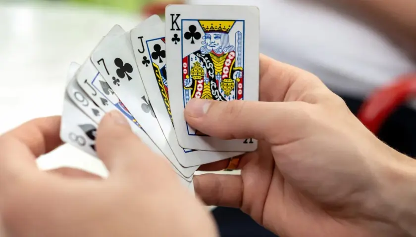 Ręce trzymają karty do gry, wśród nich Król trefl. Czy to początek emocjonującej gry w kuku?