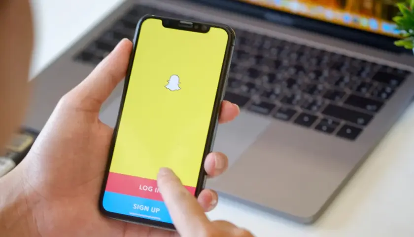 Dłoń trzyma smartfon z logo Snapchata. Widoczny ekran logowania, który może pomóc w procesie jak usunąć konto na snapie.