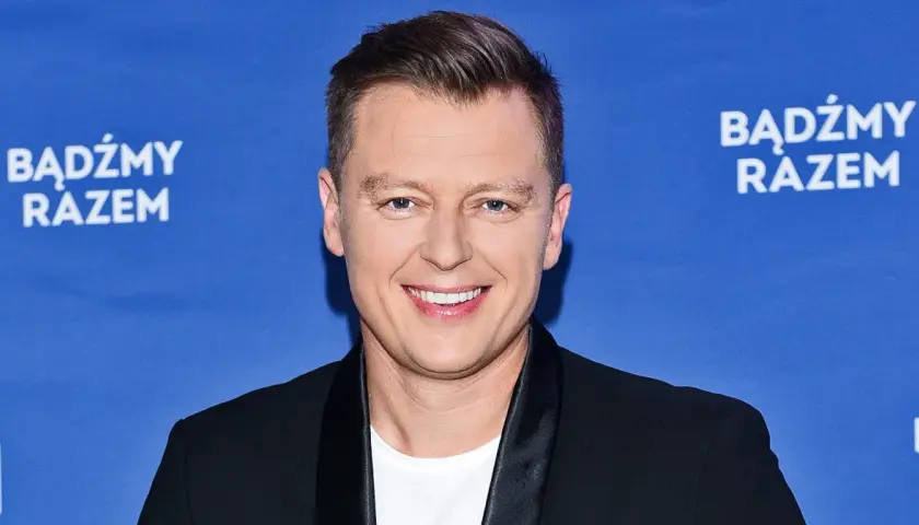 Rafał Brzozowski w czarnym garniturze na niebieskim tle z napisem "Bądźmy razem".
