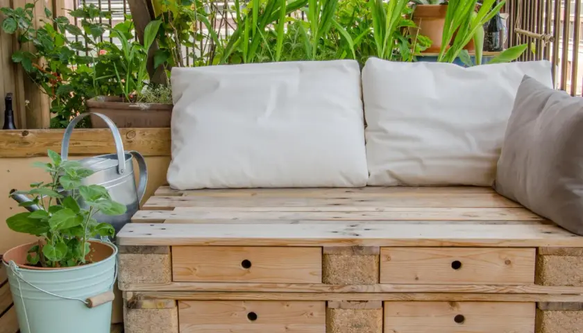 Bequeme Sitzbank aus Paletten mit Schubladen, umgeben von grünen Pflanzen. Tolle Ideen aus Paletten für Balkon und Garten.