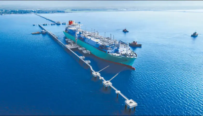 Pływający terminal LNG przycumowany do nabrzeża, z holownikami na wodzie.