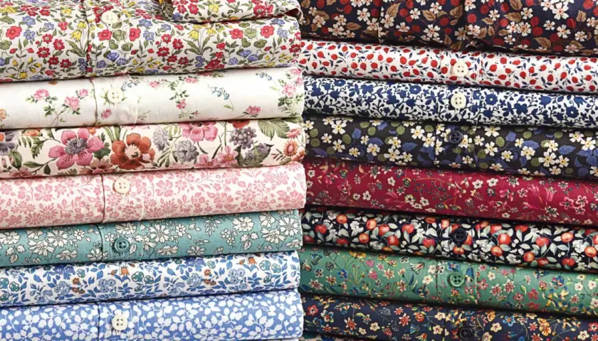 Stacks of folded shirts showcase vibrant, small floral prints, a hallmark of what is liberty fabric.