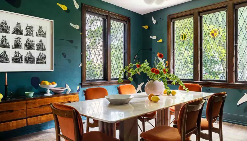 A vibrant kitchen and dining room design featuring a marble table, orange chairs, and a dark teal wall with playful accents.