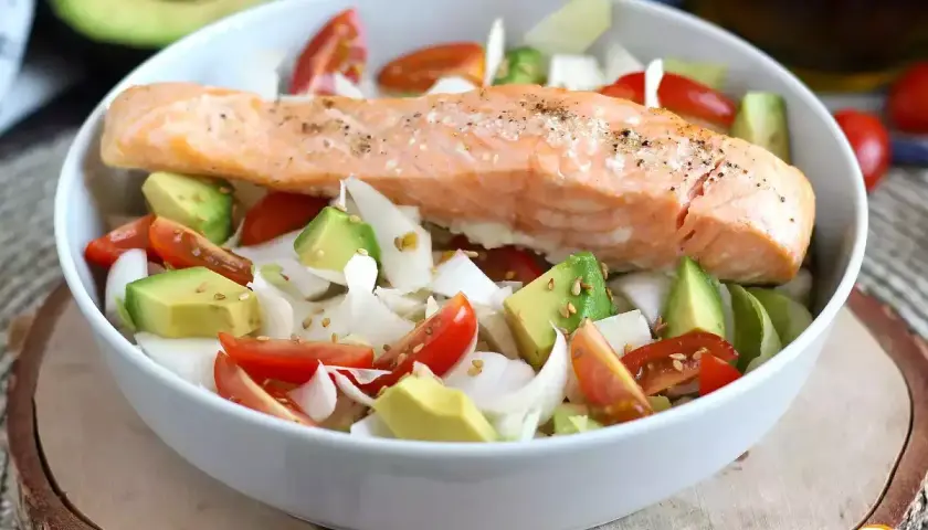 Delizioso filetto di salmone cotto su un letto di avocado, pomodorini e cipolla bianca. Un piatto leggero e gustoso, perfetto come secondi di pesce.