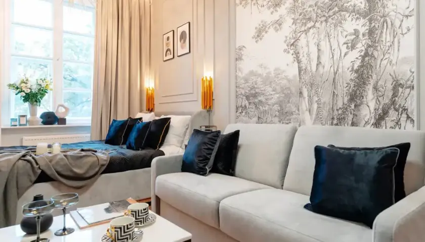 Impresjonująca dekoracja ściany nad narożnikiem z motywem leśnym. Jasna sofa i łóżko tworzą przytulną przestrzeń.