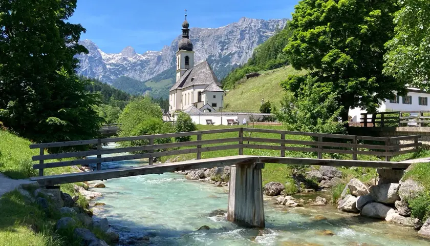 Idyllische Kirche mit Bergkulisse und Fluss – ein malerisches Motiv, das zu den beliebten Reisezielen Deutschlands zählt.