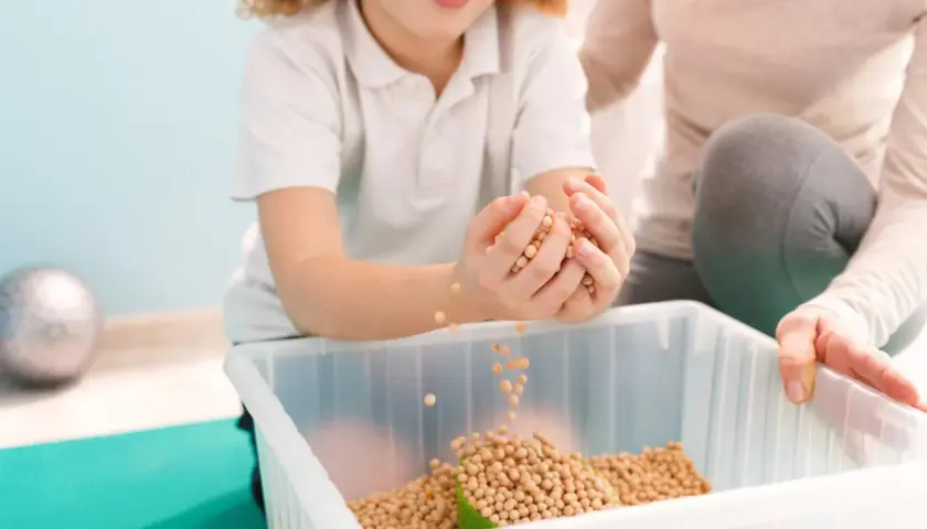Dziecko z radością przesypuje fasolki, ćwicząc zmysły. Terapia sensoryczna pomaga w rozwoju.