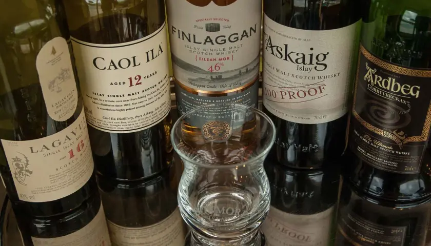 Bouteilles de whisky Islay tourbé : Caol Ila, Lagavulin, Finlaggan, Port Askaig, Ardbeg. Un verre à dégustation vide est au centre.