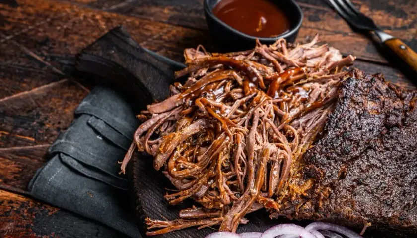 Pyszna, soczysta szarpana wołowina polana sosem BBQ, podana z krążkami cebuli na drewnianej desce.