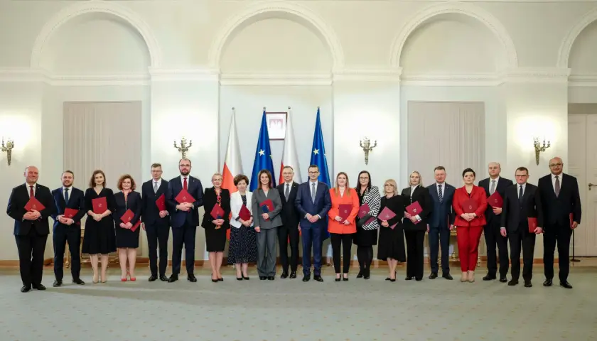 Grupa osób w eleganckich strojach, z flagami Polski w tle. Czy wśród nich jest premier Polski?