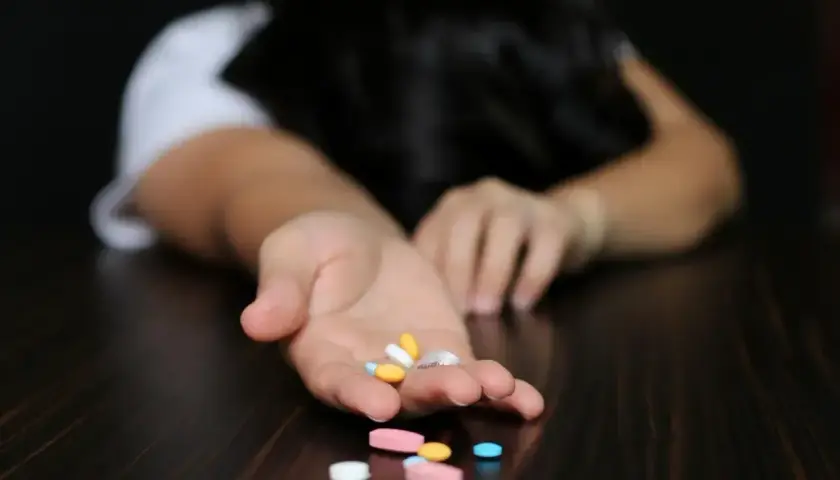 Dłoń z garścią tabletek, w tym alprazolam, na ciemnym blacie.