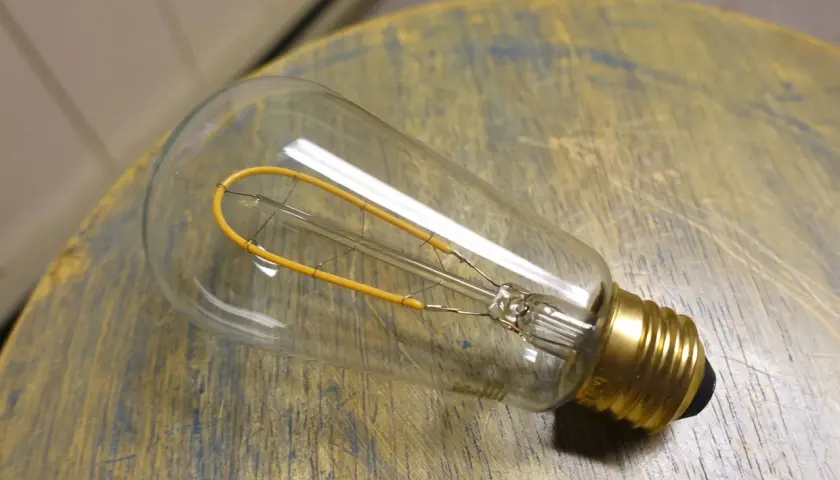 Bombilla de filamento regulable, con un diseño vintage y un filamento amarillo en forma de bucle, descansa sobre una superficie de madera desgastada.