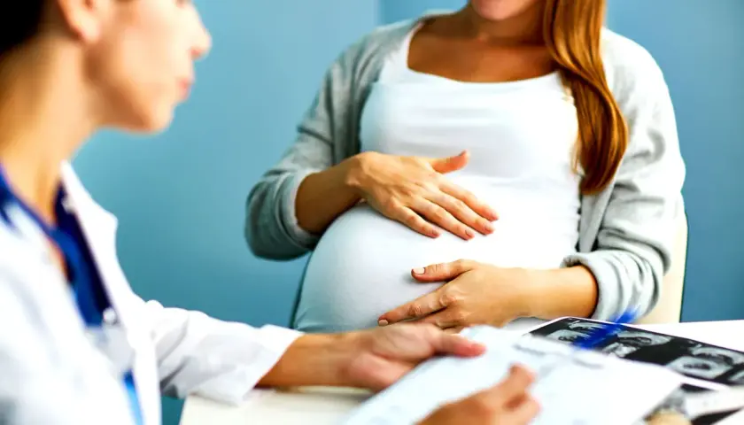 Medico spiega a donna incinta quando si fa la villocentesi, con ecografie sul tavolo.