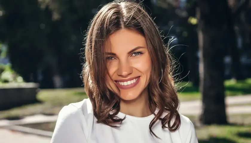 Uśmiechnięta brunetka w białej koszulce, idealna do zadawania pytań do nowo poznanej osoby.