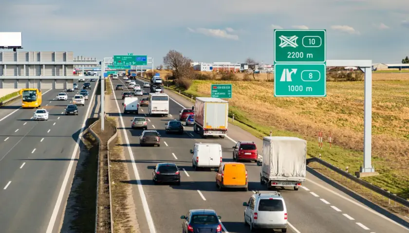 Ruch na autostradzie w Czechach, z samochodami i ciężarówkami pędzącymi z dużą prędkością. Znaki drogowe wskazują kierunki i odległości.