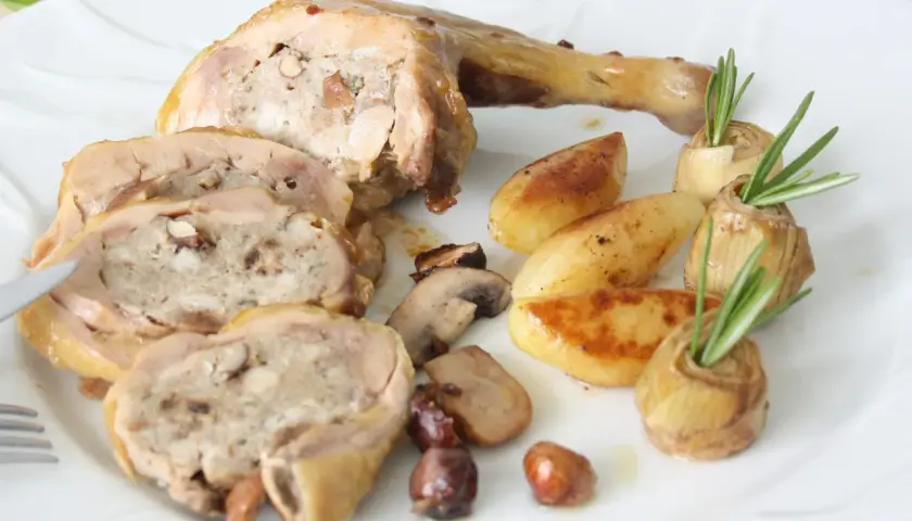 Délicieuse cuisse de pintade farcie, servie avec des pommes de terre rôties, des champignons et des cœurs d'artichauts garnis de romarin.