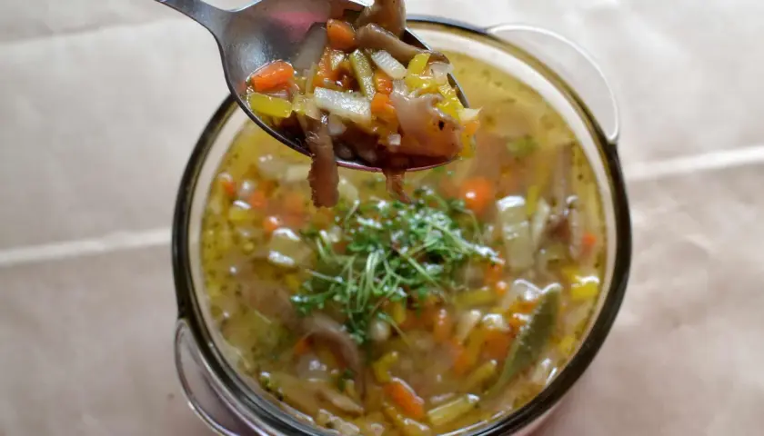 Łyżka pełna aromatycznych flaków z boczniaków, z marchewką i selerem, nad miską pełną tej pysznej zupy.