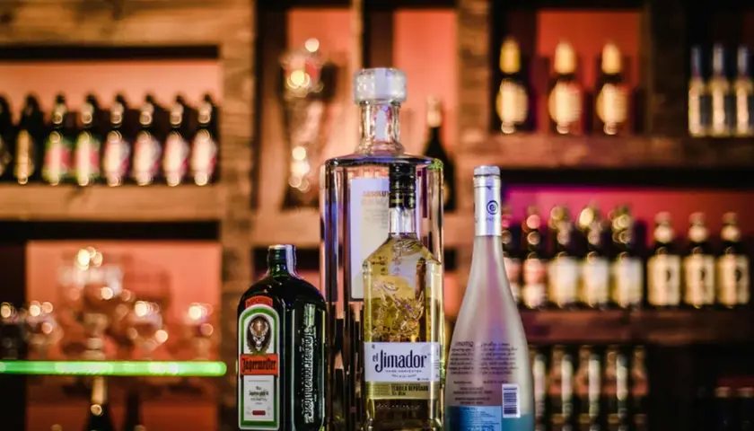 Butelki alkoholu: Jägermeister, El Jimador, Absolut i Hypnotiq na tle półek z napojami.