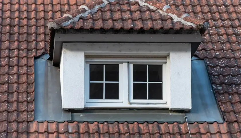 Dachgaube mit zwei Fenstern, umgeben von roten Dachziegeln. Die Bleiverkleidung zeigt, wie man eine dachgaube richtig abdichten kann.