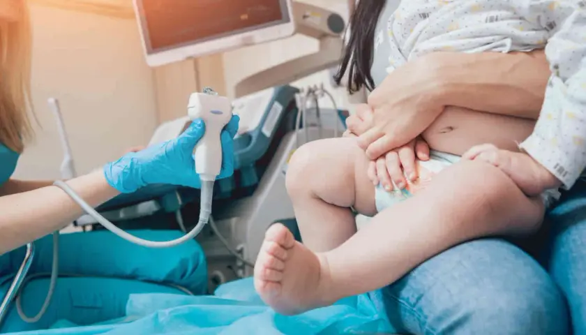 Lekarz wykonuje usg przezciemiączkowe u niemowlaka. Dziecko siedzi na kolanach rodzica, a lekarz trzyma sondę aparatu USG.