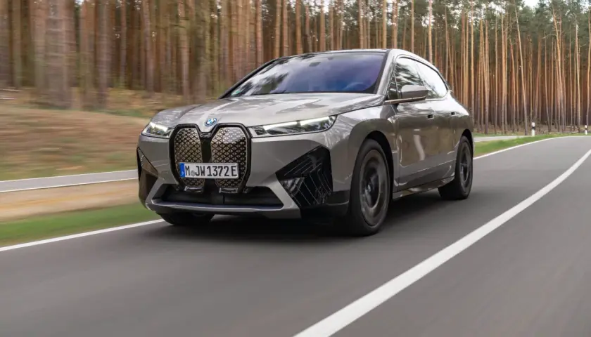 Szary BMW iX jedzie po drodze wśród drzew.