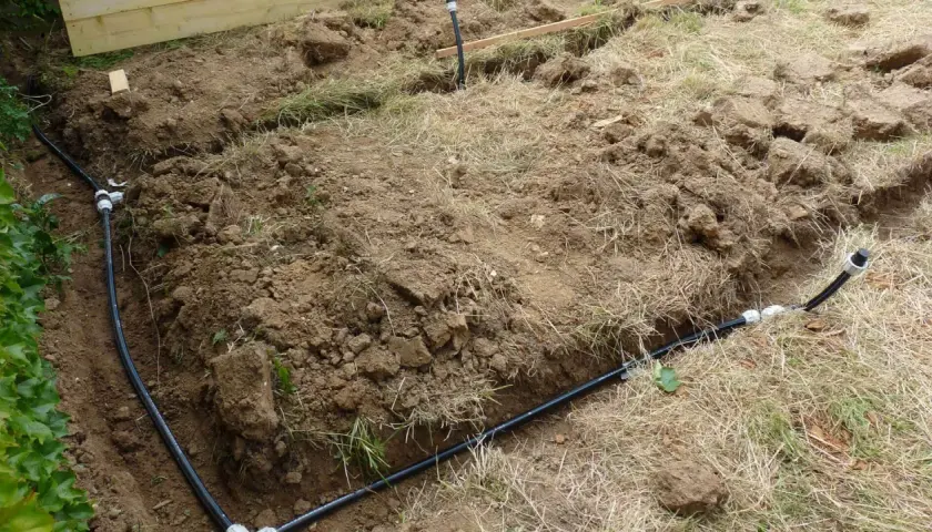 Des tranchées creusées révèlent des tuyaux noirs, prémices de réseaux enterrés pour l'irrigation ou le drainage.