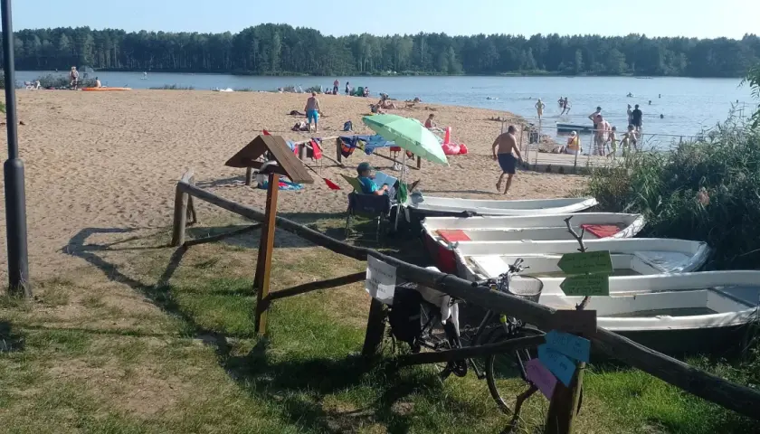Słoneczny dzień nad zalewem zielona. Ludzie odpoczywają na plaży, kąpią się, a obok stoją łódki.