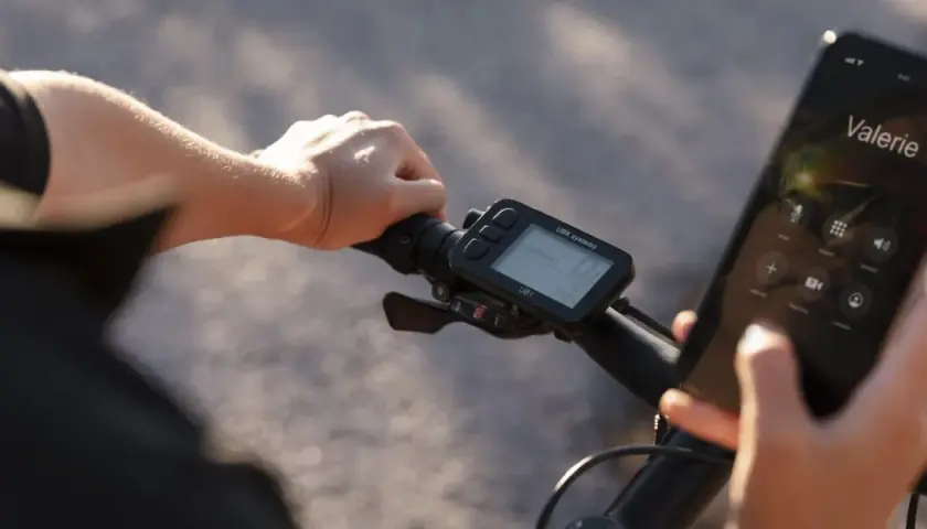 Rowerzysta trzyma kierownicę, na której zamontowany jest licznik rowerowy nie pokazuje prędkości. Obok wyświetlacz telefonu z połączeniem do Valerie.