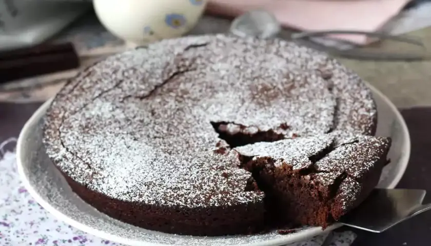 Un délicieux gâteau au chocolat saupoudré de sucre glace, parfait pour une recette gâteau au chocolat facile. Une part est coupée.