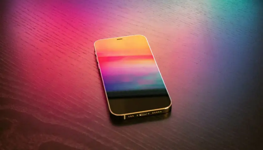 Złoty iPhone z kolorowym ekranem na drewnianym blacie. Dowiedz się, jak wgrać dzwonek na iPhone bez iTunes.