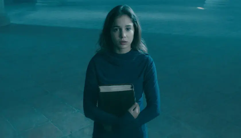 Alba Baptista, med en gammal bok i famnen, ser fundersam ut i det blåa ljuset.
