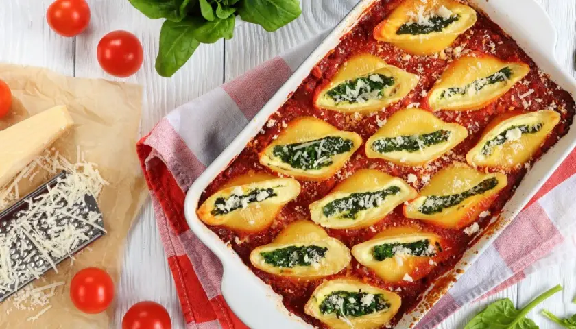 Makaron conchiglioni faszerowany szpinakiem i serem w sosie pomidorowym, podany w naczyniu żaroodpornym.