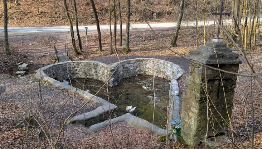Kamienny krzyż i sercowate źródełko w dolinie Eliasówki, otoczone lasem i opadłymi liśćmi.