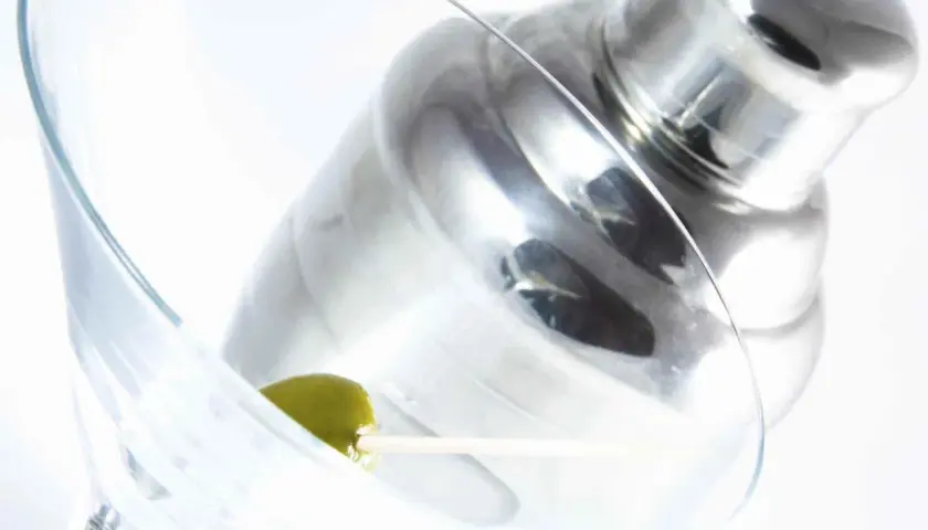 Verre à martini avec une olive, prêt pour une recette de martini gin. Shaker à cocktail en arrière-plan.