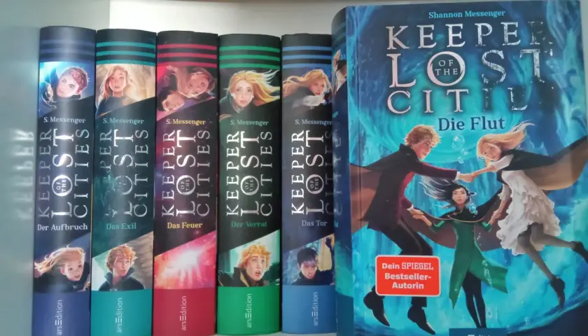 Die Bücherreihe "Keeper of the Lost Cities" mit Sophie als Hauptfigur. Mehrere Bände sind nebeneinander aufgestellt, der größte Band "Die Flut" steht rechts.