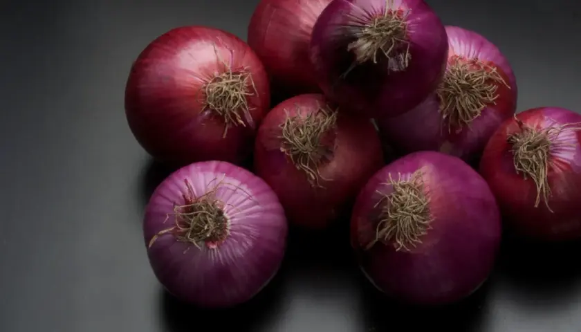 Un grupo de cebollas rojas sobre fondo oscuro. Se rumorea que el champú de cebolla tiene propiedades beneficiosas para el cabello.