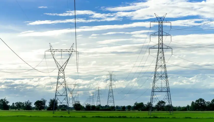 Wysokie słupy energetyczne na zielonej działce, ciągnące się w dal pod błękitnym niebem z chmurami.