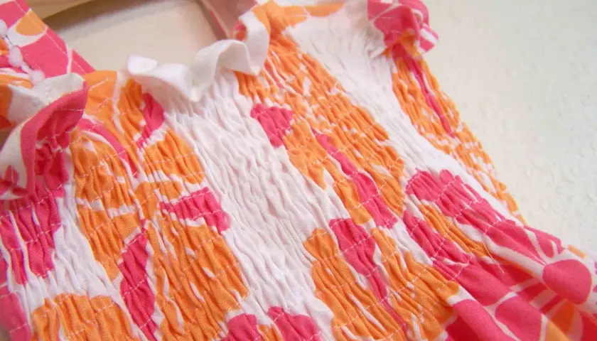 Close-up of a smocked garment with a floral pattern, showing how to sew with elastic thread for a gathered effect.