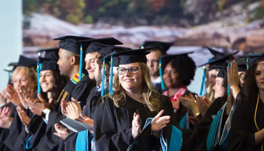 Graduates in caps and gowns applaud, celebrating their achievements in the UNC Chapel Hill online MPA program.