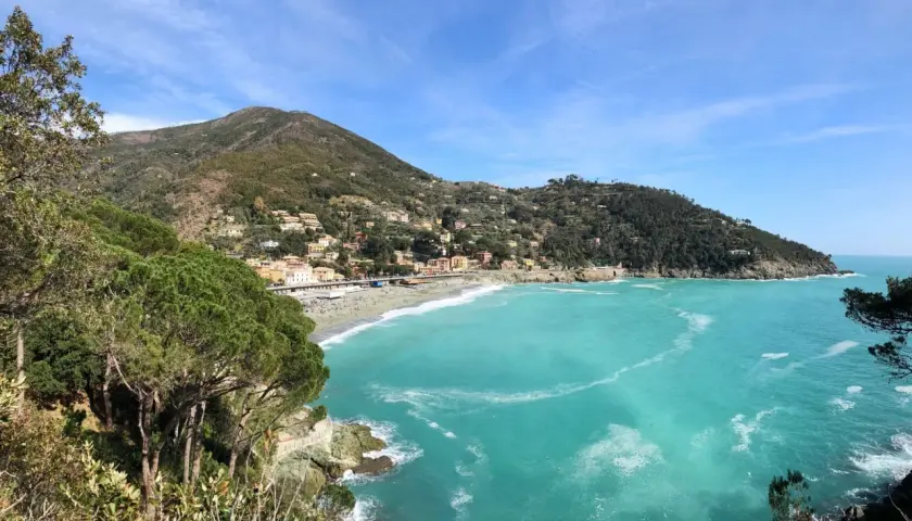Vue panoramique de la baie de Bonassola en Italie, avec ses eaux turquoise, sa plage animée et ses collines verdoyantes couvertes de maisons.