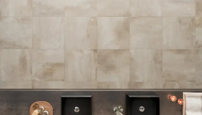 Bagno moderno con due lavabi neri, accessori e un rivestimento in gres tutta massa effetto pietra.