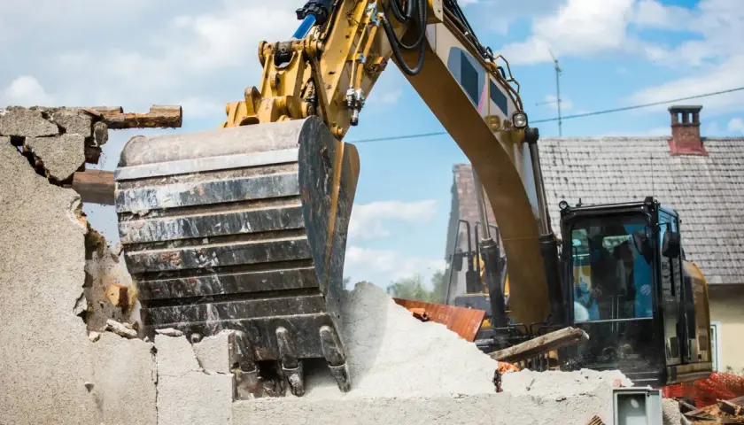 Une pelleteuse jaune démolit une maison. Le prix de la démolition maison est en cours de calcul.