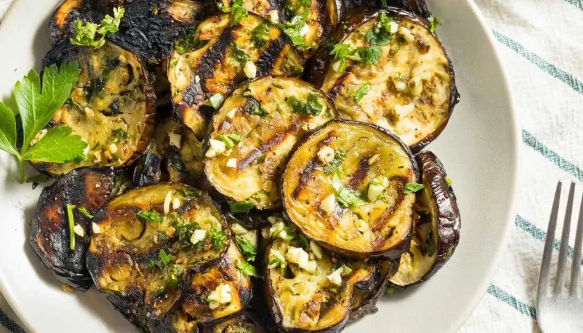 Rodajas de berenjenas a la plancha, doradas y tiernas, con ajo picado y perejil fresco. Un plato sencillo y delicioso.