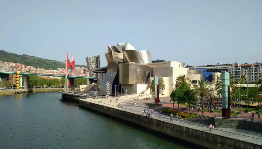 Museo Guggenheim y puente rojo, ideal para saber qué ver en Bilbao en 1 día. Paseo junto a la ría con gente disfrutando del sol.